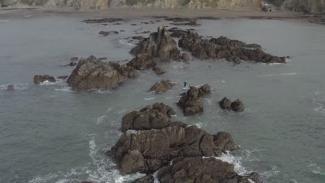 Aerial-of-skillful-SUP-paddleboarder-paddling-among-craggy-ocean-rocks