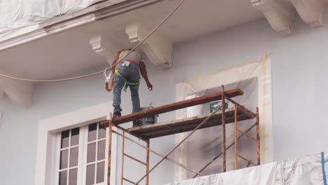 Professional-worker-standing-over-a-scaffold-with-a-bucket-painting-the-exterior-of-a-beautiful-building-with-hispanic-architecture-during-a-hot-sunny-summer-day-in-Panama-City's-Casco-Viejo