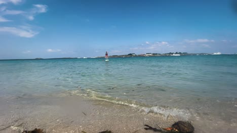 Blick-Auf-Den-Wunderschönen-Strand-Auf-Der-Insel-Saint-Nicolas,-Im-Hintergrund-Ein-Typ,-Der-Auf-Einem-Paddel-Reitet