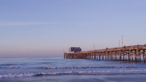 Olas-Del-Océano-En-La-Costa-De-La-Playa-Con-Muelle-De-Pesca-Al-Amanecer-En-Newport-Beach,-California,-EE.UU.