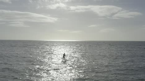 Einsamer-Stand-Up-Paddleboarder-Ist-Im-Sonnenstrahl-Auf-Dem-Unruhigen-Ozean-Silhouettiert