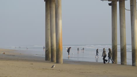 Two-girls-walking-under-the-pier-in-Huntington-Beach,-California