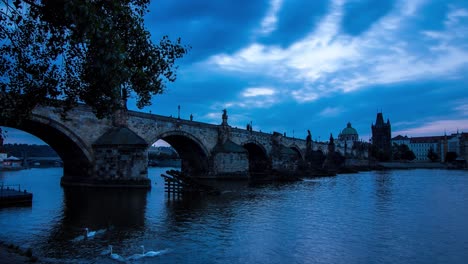 Blue-morning-timelapse-of-the-Charles-Bridge-in-Prague,-Czech-Republic-next-to-the-Vltava-river-with-panoramic-view-of-the-river-shore