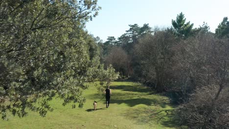Caucasian-Woman-With-Her-Dog-On-Leash-Jogging-Through-Trees-In-Cres,-Croatia-On-A-Sunny-Morning