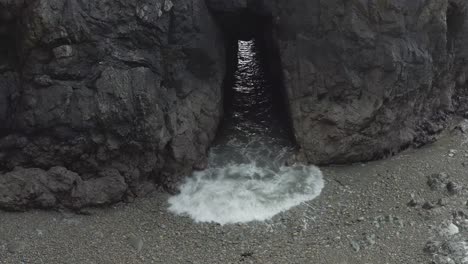 Tunnel-in-rocky-shore-islet-allows-grey-ocean-waves-to-surge-through