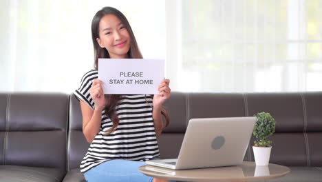 Asian-Woman-social-distancing-covid-19-campaign-holding-stay-at-home-paper-page-in-Apartment-interior