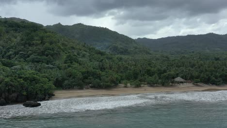 Aerial-view-of-tropical-sandy-beach-with-green-mountains-in-background-during-cloudy-grey-day---Playa-El-Valle,Dominican-Republic