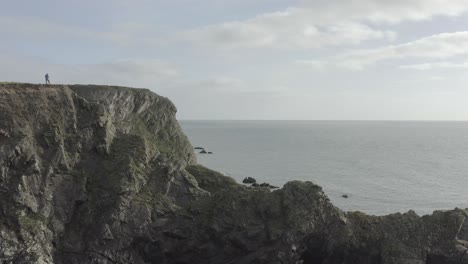 Static-shot-of-drone-pilot-atop-steep-rock-cliffs-overlooking-ocean