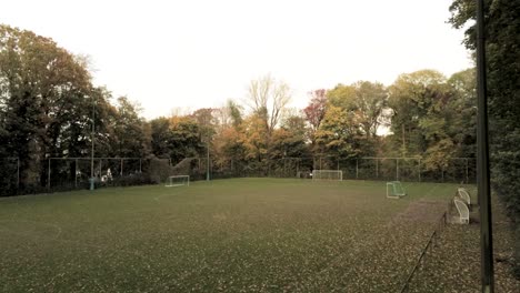 Flying-through-the-broken-fence-of-the-soccer-field-in-the-middle-of-a-lush-hidden-autumn-forest---Aerial-tracking-shot
