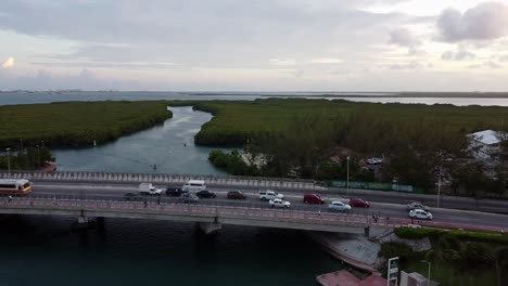 Zoom-out-of-a-bridge-above-of-underpass-lagoon-while-car-driving-at-sunset-time