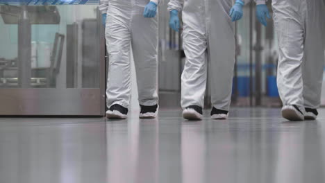 Three-scientists-dressed-in-full-protective-equipment-walk-towards-camera-inside-a-laboratory