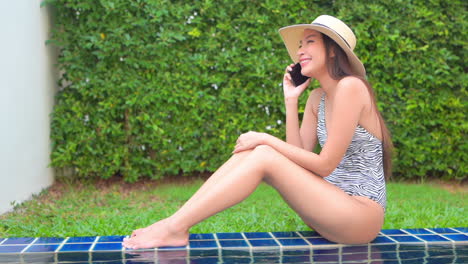 Sexy-Asian-Woman-in-Swimsuit-Talking-on-Smartphone-by-the-Pool,-Full-Frame