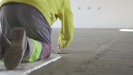Static-view-of-a-labourer-levelling-the-plastered-floor-using-flat-trowel-and-cement-manually-wearing-a-neon-jacket-and-grey-pants