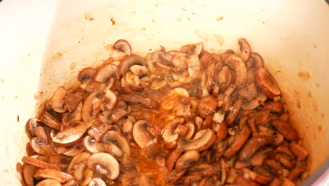 Sautéing-mushrooms-in-an-enamel-Dutch-oven-pot---mushrooms-frying-and-bubbling-on-the-stove---close-up-top-down-view