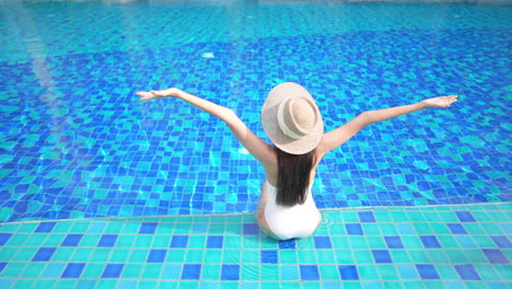 A-healthy,-fit-woman-sits-on-the-edge-of-a-swimming-pool-as-she-stretches-her-arms