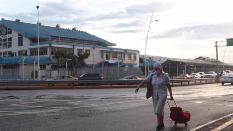 Panama-City's-Seafood-Market-near-Balboa-Avenue's-wet-asphalt-streets-where-citizens-in-vehicles-transit-from-and-towards-their-workplace-and-a-lady-wearing-a-facemask-rolls-a-bag-crossing-the-frame