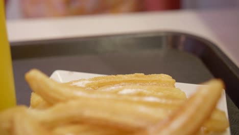 Close-up-on-fried-churros-in-plate-with-juice-in-glass