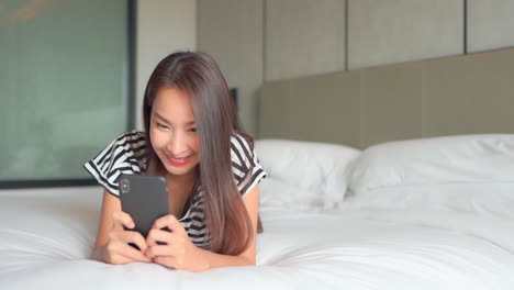 Mujer-Asiática-Atractiva-Usando-Chat-De-Teléfono-Móvil-En-Una-Cama-En-Casa-Por-La-Mañana