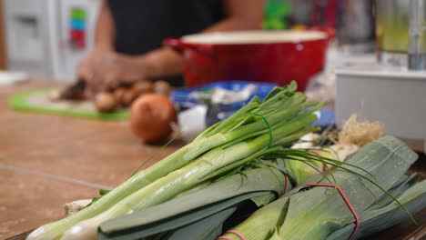 Leeks-in-the-foreground-then-a-focus-pull-to-a-woman-slicing-mushrooms-for-a-homemade-soup-recipe