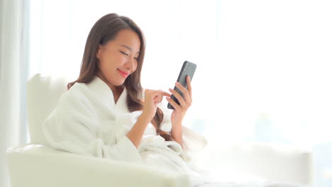 Beautiful-Exotic-Woman-in-Bathrobe-by-Window-Checking-Messages-on-Smartphone