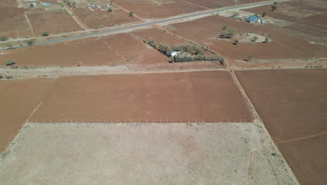 Luftaufnahme-Einer-Trockenen-Landschaft-Im-Ländlichen-Kenia,-Die-Ein-Kleines-Dorf-In-Der-Ferne-Enthüllt