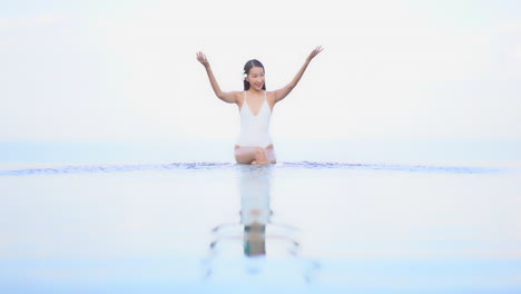 Slender-Asian-Woman-in-Infinity-Pool-Playing-and-Spraying-Water,-Slow-Motion
