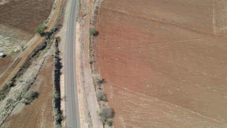 Drone-flying-over-motorway-in-rural-Kenya,-tilting-up-and-revealing-three-motorcyclists-driving-over-street