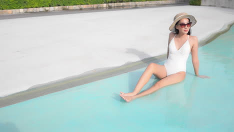 A-young-woman-in-a-white-bathing-suit-lounges-in-the-shallow-end-of-the-pool