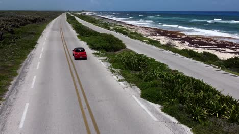 Aerial-View-of-a-Red-Car-Driving-Down-on-a-Beach-Highway-in-Cozumel