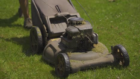 Close-up-tracking-shot-of-male-person-mowing-lawn-with-old-mower-during-sunny-day---4K-low-angle---Working-in-own-garden