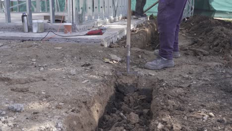 Close-up-shot-of-labor-man-digging-hole-with-shovel-on-construction-site---4k-track-shot