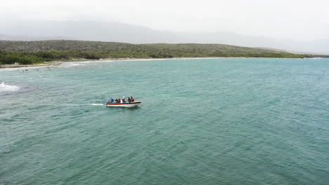 AERIAL---People-on-tour-boat,-Monte-Rio-beach,-Dominican-Republic,-truck-right