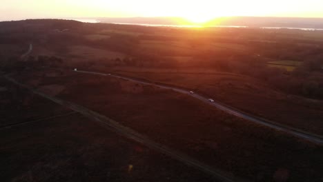 Aerial-forward-shot-over-Woodbury-Common-in-Devon-England-and-a-busy-road-with-the-sun-going-down