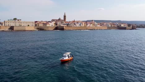 Clip-of-a-lonely-boat-in-the-sea-in-front-of-castle-walls-of-the-Alghero-town-in-Sardinia,-Italy