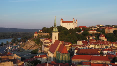 Wide-rotating-drone-shot-with-the-Saint-Martin's-Cathedral-in-the-foreground-and-the-Bratislava-Castle-in-the-background-in-Bratislava-Slovakia-during-the-setting-sun