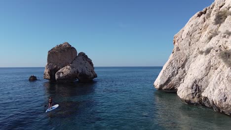 Scenic-view-of-a-woman-paddleboarding-by-large-rocks-in-the-Mediterranean-Sea