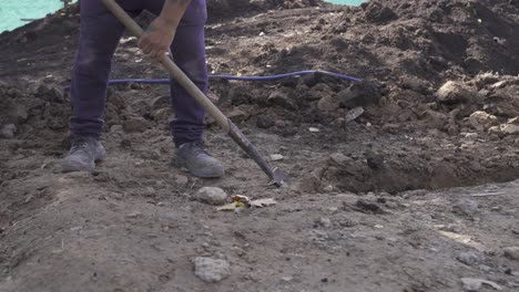 Close-up-low-angle-of-labor-man-with-shovel-digging-hole-outside-on-construction-site---4K