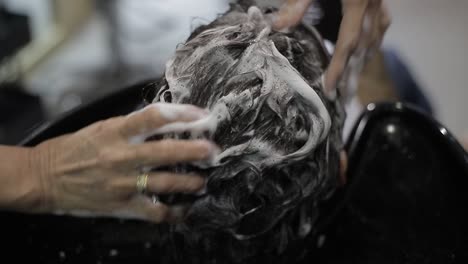 Young-girl-lying-on-salon-sink-having-her-hair-washed-by-professional-hairdresser