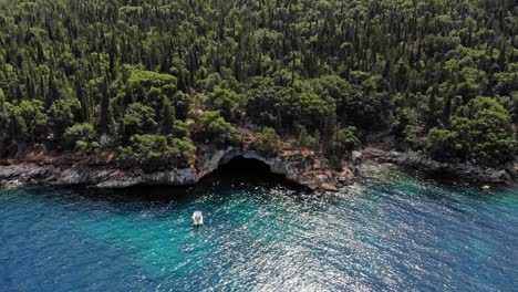Aerial-View-Of-A-White-Boat-Near-The-Forested-Seashore-In-Foki-Beach,-Kefalonia,-Greece