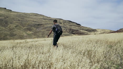 Man-walking-through-golden-grass-field-with-backpack-on,-slow-motion