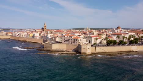 The-scenic-town-of-Alghero-in-Sardinia,-Italy-shot-from-a-drone-from-outside-the-castle-walls-with-a-cathedral-and-the-old-town-in-the-background