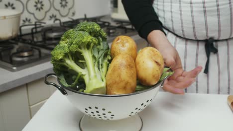 Chef-showcases-vegetarian-ingredients:-greens,-broccoli-and-potatoes-on-kitchen-table