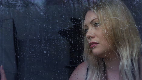 Sad-lonely-young-blonde-woman-looking-out-of-a-window-in-the-rain