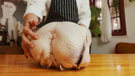Chef-places-big-turkey-on-wooden-kitchen-table-in-authentic-stylized-kitchen