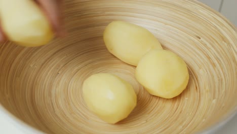 Chef-puts-peeled-potatoes-into-deep-wooden-bowl
