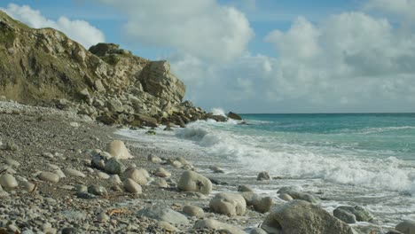 4K-Slow-motion-cinematic-shot-of-waves-hitting-rocks-on-a-beach,-at-Church-Ope,-Portland-Dorset,-in-England,-on-a-sunny-day,-with-cliffs-in-the-background