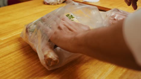 Close-up-on-chef-hands-putting-herbs,-salt-and-spice-into-plastic-packing-with-turkey-meat