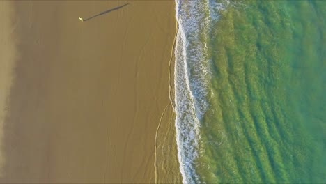 Aerial-shot-looking-directly-down-and-offering-a-bird's-eye-view-of-the-crystal-clear-aquamarine-waters-off-the-beach-of-Fraser-Island,-and-over-the-sands-and-tire-tracks-from-4x4-trucks