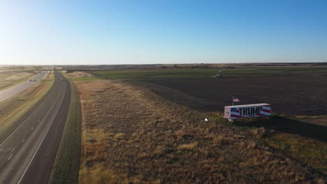 Aerial-Drone-Video-Donald-Trump-2024-Presidential-Election-Campaign-Sign-Painted-on-a-Large-Truck-or-Trailer-with-Cars-Driving-on-Highway-in-Rural-Farm-Land-with-Oil-Rig-in-the-Middle-of-Nowhere