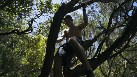 Dolly-shot-passing-under-shirtless-young-man-in-tree-overhead,-slow-motion